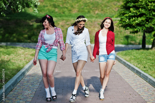 Three happy girls in short shorts and wreaths on heads walking d