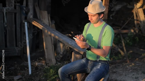 Young man holding a cellphone at sunset. A man sits at the sawmill
