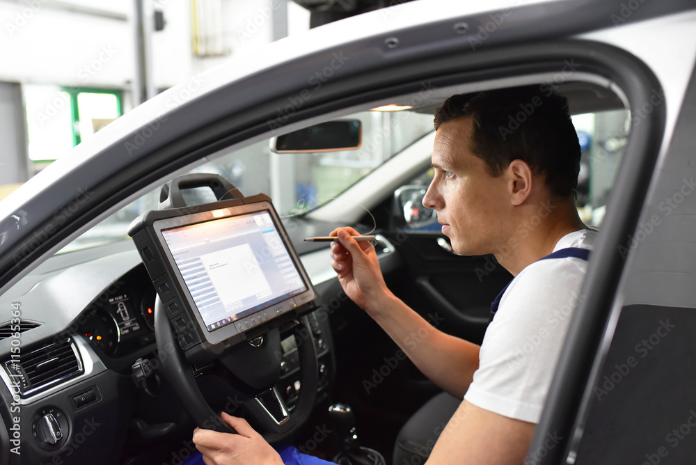 Automechaniker mit Diagnosecomputer in einer Werkstatt - auslesen des Fehlerspeichers in der modernen KFZ Diagnose