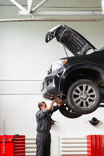 Canvas Print Mechanic working under raised car in service station