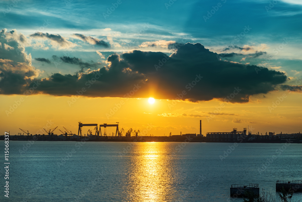 sunset in dark clouds over river and shipbuilding factory