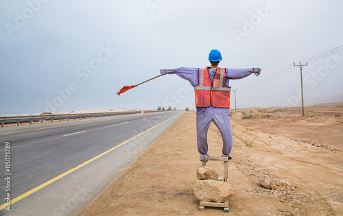 mannequin dressed in safey clothing with a red warning flag standing on the side of the road in Salalah Oman photo