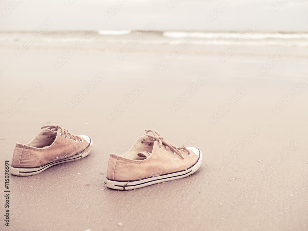 Naklejka premium Yellow vintage canvas shoes on the sand beach