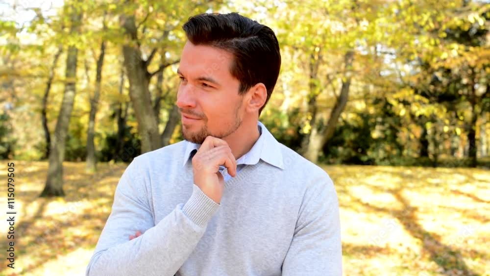 Young handsome man stands in the woods, strokes his chin, looks satisfied and thinks about something Young handsome man stands in the woods, strokes his chin, looks satisfied and thinks about something