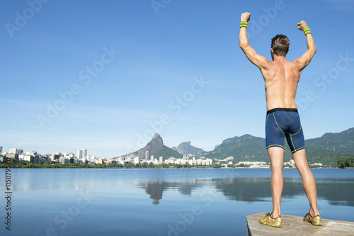 Athlete in blue compression shorts standing with champion arms raised in front of Rio de Janeiro, Brazil skyline at Lagoa Rodrigo de Freitas lagoon
