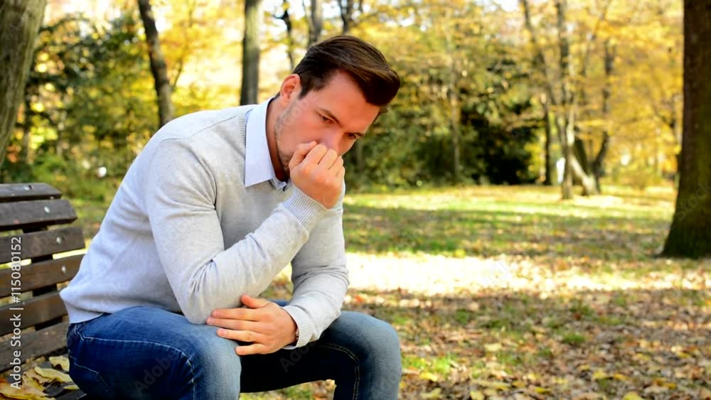 Young man sits on bench in a park, is nervous, sad and thinks Young man sits on bench in a park, is nervous, sad and thinks