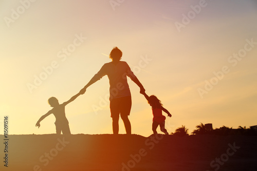 father with son and daughter silhouettes play at sunset