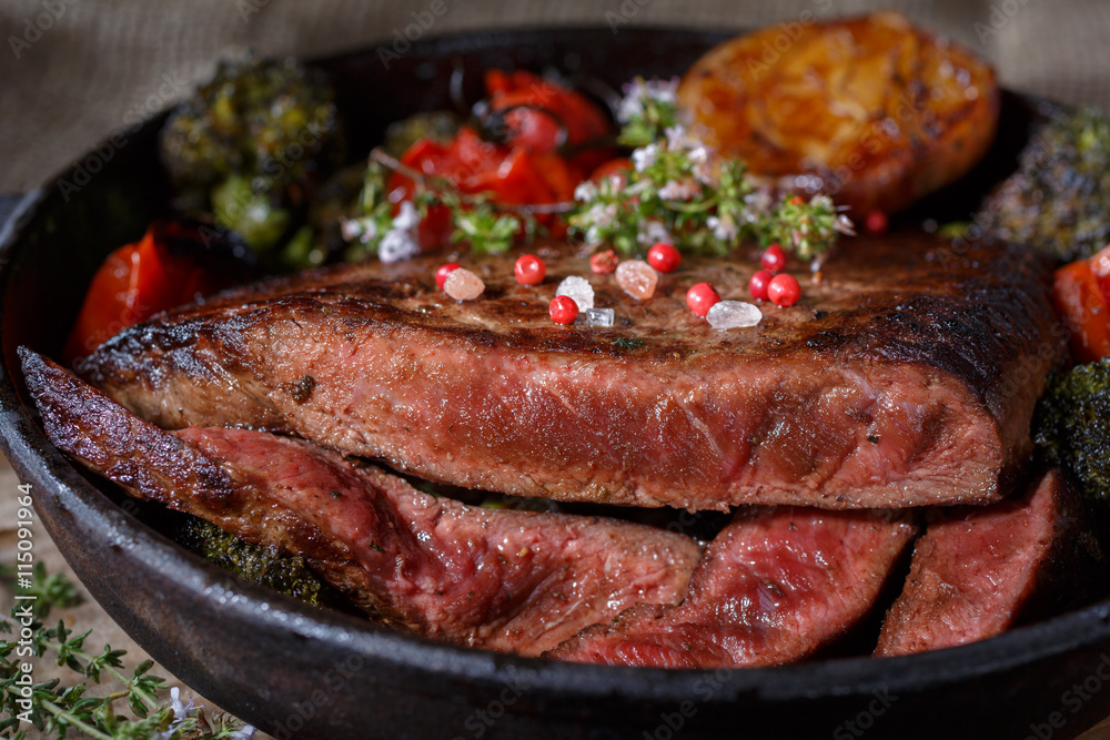 Beef steak medium rare with vegetables on a cast iron skillet. Still life of meat and vegetables in a low key. Rustic style food. covered with a rustic table