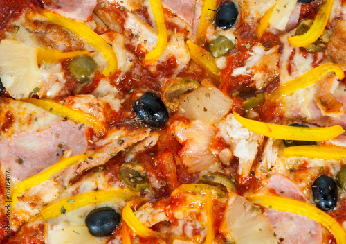 Hawaiian pizza with pineapple, ham, chicken, cheese, olives and vegetables on a wooden table