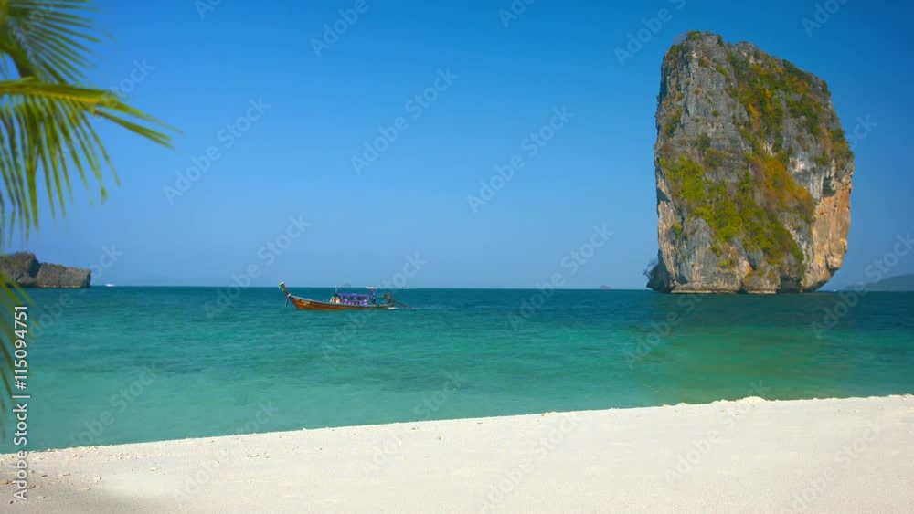 Video 3840x2160 - Wooden tour boat cruises past a massive limestone formation and a pristine, white sand beach at Railay Beach in southern Thailand. Video 3840x2160 - Wooden tour boat cruises past a massive limestone formation and a pristine, white sand beach at Railay Beach in southern Thailand.