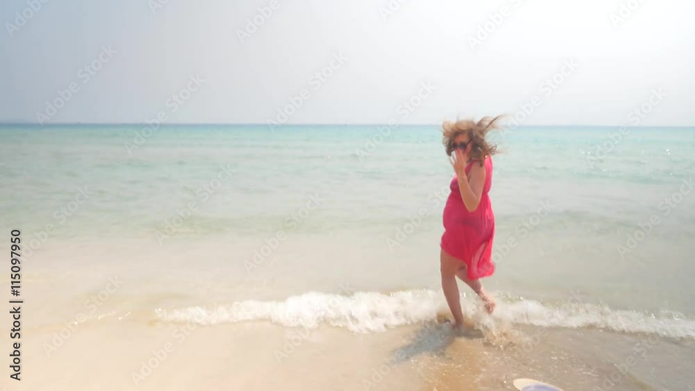 Smiling pregnant woman running into the sea water and losing the hat. Dolly in shot Smiling pregnant woman running into the sea water and losing the hat. Dolly in shot