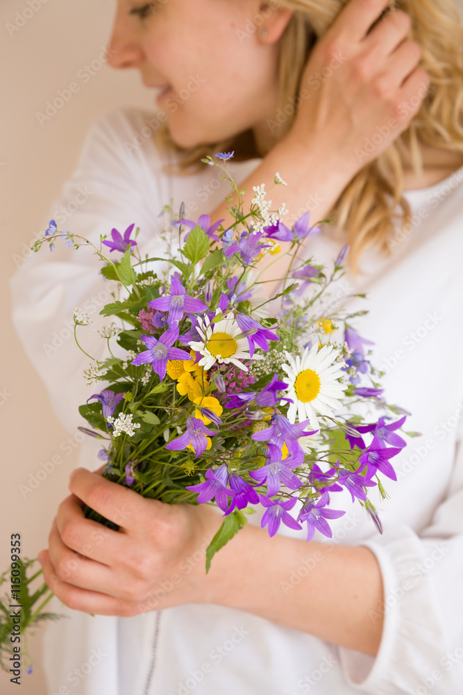 Closeup of woman's hands holding beautiful bunch of wild flowers. Girl with summer bouquet at white wall