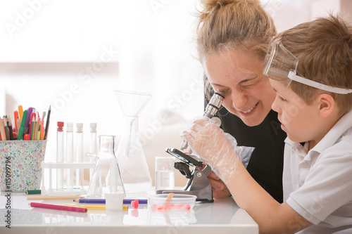 Young mother and elementary school kid boy looking into microscope at home. Family studying samples under the microscope. Science activities with children. Preparing for science lesson. photo