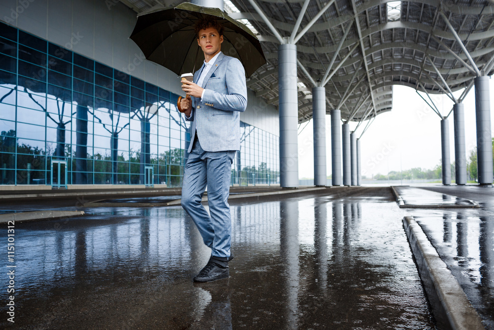 Handsome redhaired businessman with umbrella drinking coffee