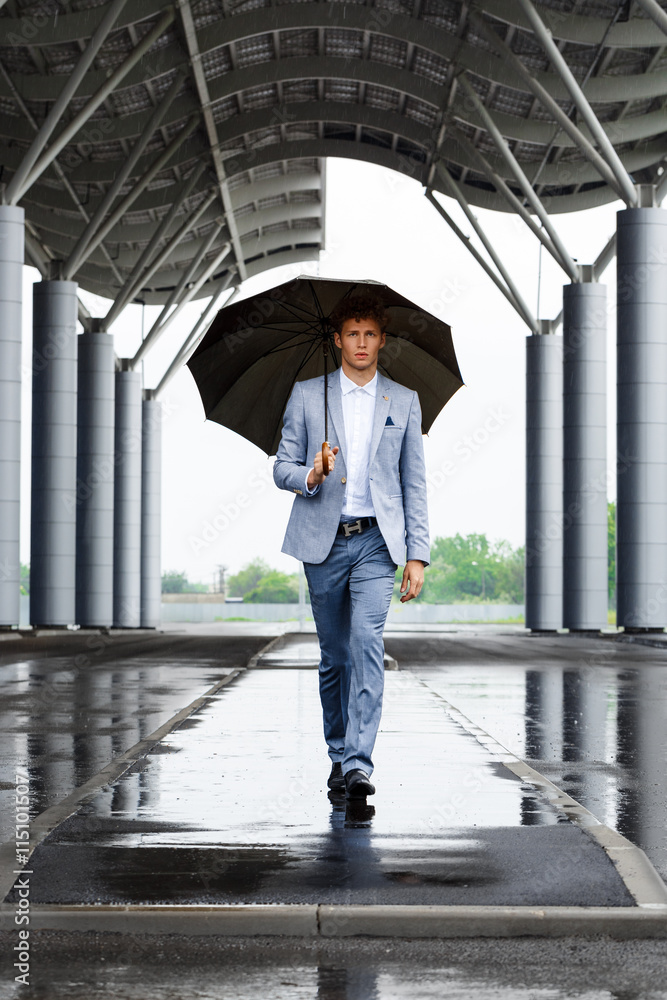 Picture of handsome young redhaired businessman holding umbrella walking on street