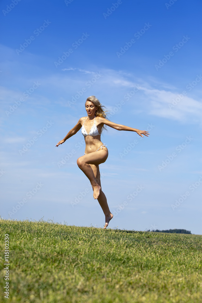 The happy woman in white bikini jumps in a summer green field against the blue sky. The happy woman in white bikini jumps in a summer green field against the blue sky.