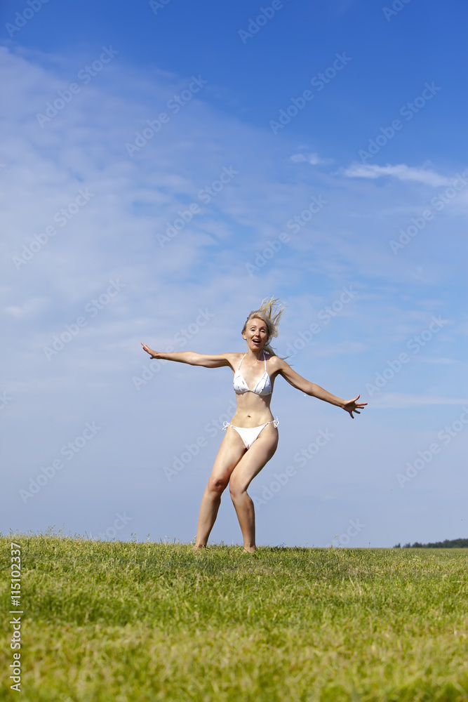 The happy woman in white bikini jumps in a summer green field against the blue sky. The happy woman in white bikini jumps in a summer green field against the blue sky.