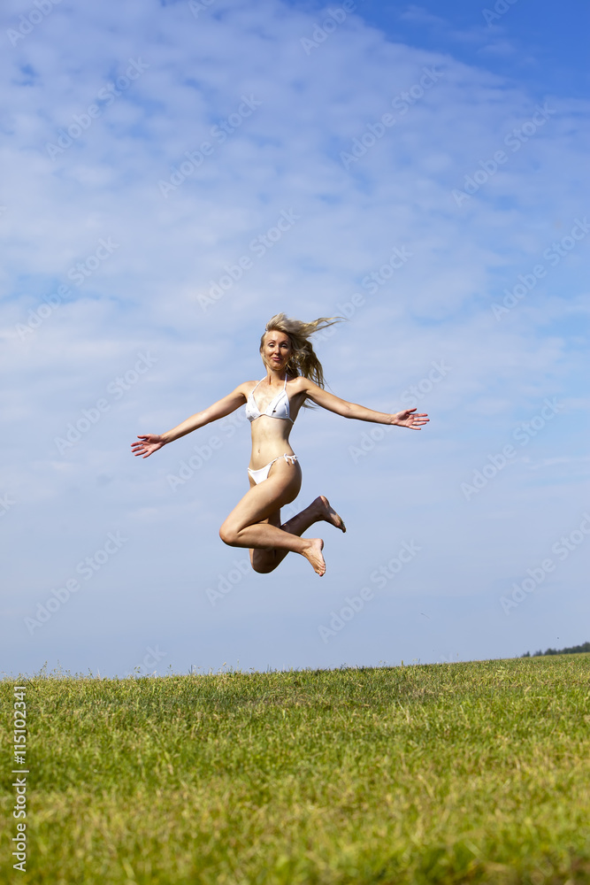 The happy woman in white bikini jumps in a summer green field against the blue sky. The happy woman in white bikini jumps in a summer green field against the blue sky.