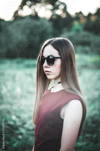 Young, beautiful girl in a red dress walking in nature, in the field. Beautiful girl holding flowers, daisies. Sunglasses.
