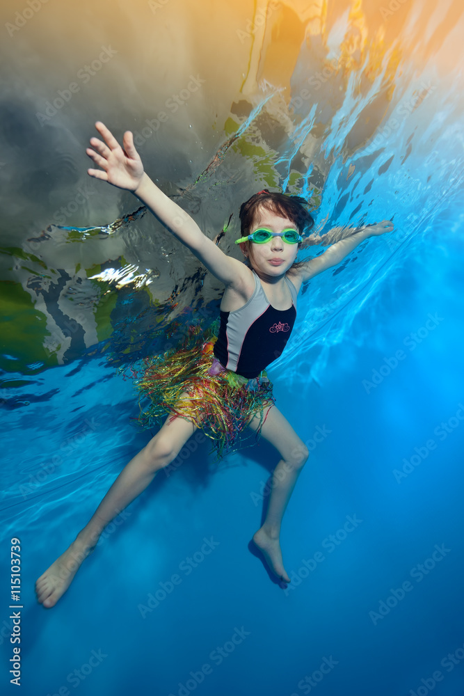 Happy little girl swimming and playing underwater in the pool on a blue background. Portrait. Bottom view. Vertical orientation