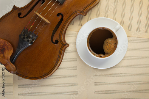 old violin and white coffee cup on musical sheets