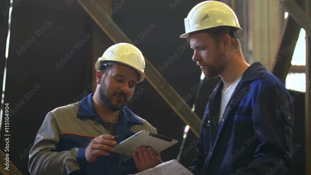 Two engineers in hardhats discussing in front of welding process Two engineers in hardhats discussing in front of welding process
