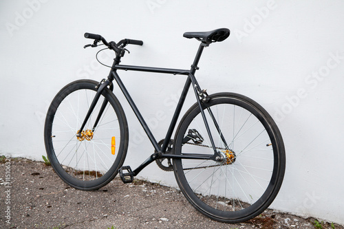 Black fixed-gear bicycle standing near gray wall