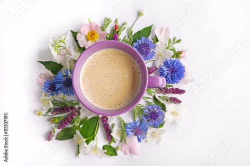 Cup of coffee with fresh flowers lying around on white background
