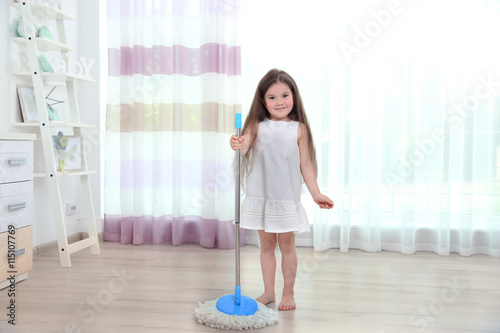 Cute little girl washing floor in room