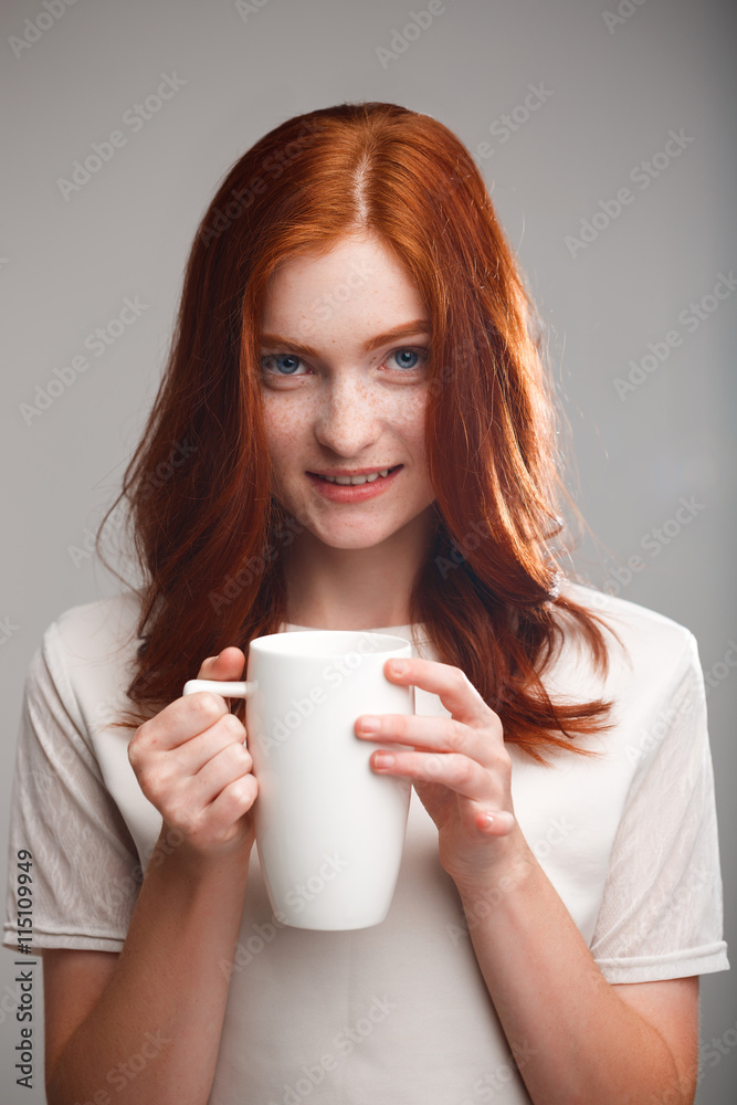 Portrait of beautiful ginger girl holding cup over gray background with back light. Portrait of beautiful ginger girl holding cup over gray background with back light.