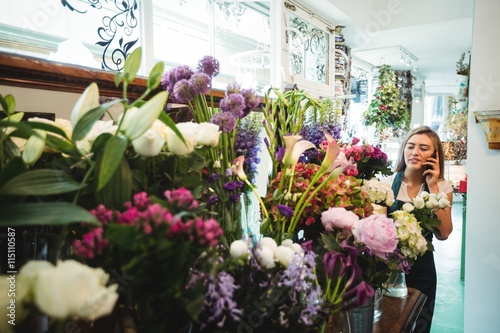 Female florist talking on mobile phone while arranging flowers photo