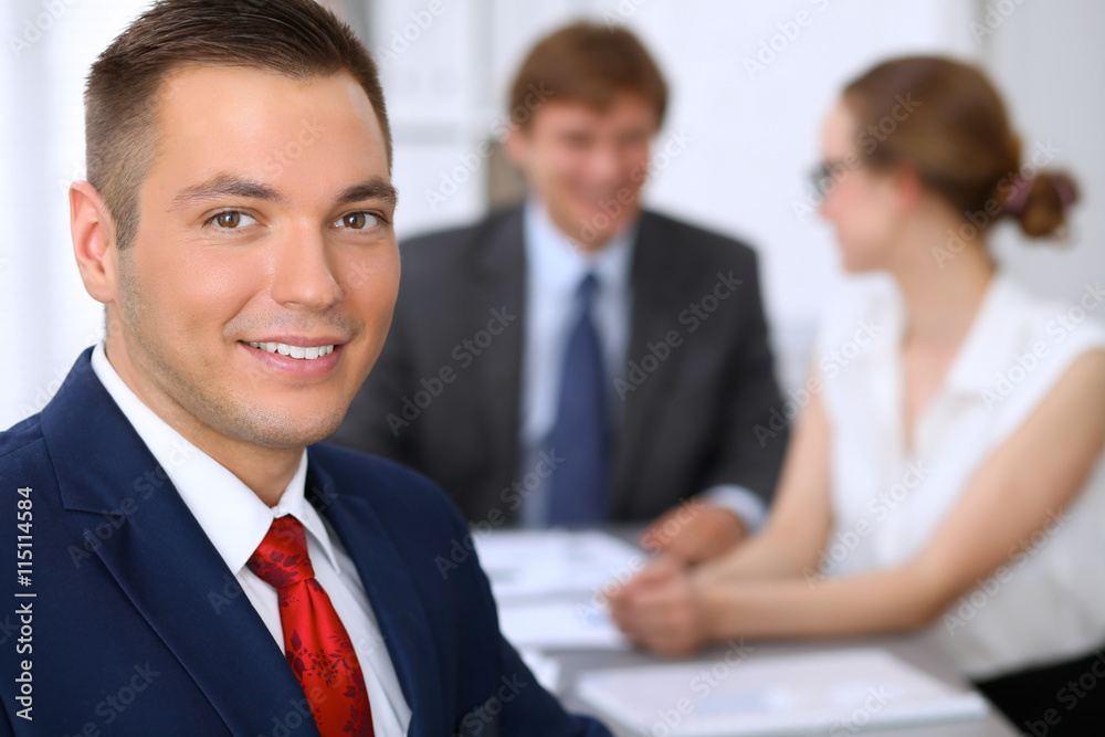 Portrait of cheerful smiling business man against a group of business people at a meeting. Portrait of cheerful smiling business man against a group of business people at a meeting.