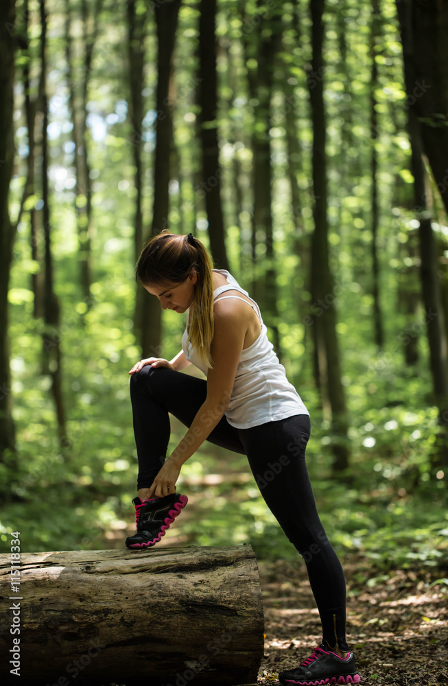 sporty girl in the woods is warming up near a big log