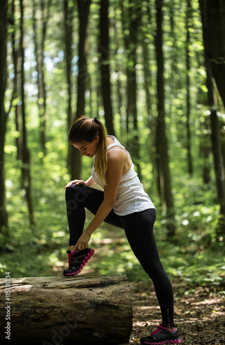 sporty girl in the woods is warming up near a big log