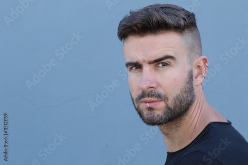 Handsome stylish young man with undercut hairstyle, beard and piercings with copy space 