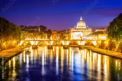 Rome skyline at night with San Pietro basilica or Saint Peter cathedral with Sant'Angelo bridge reflected on Tevere river illuminated by city lights of Roma in Italy. © bennymarty