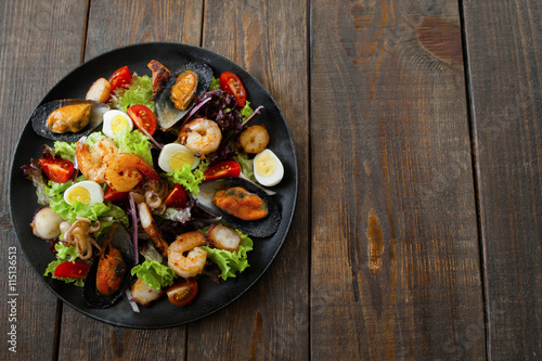 Grilled seafood salad on wood flat lay copyspace. Top view on black plate with salad with grilled seafood and quail eggs, free space