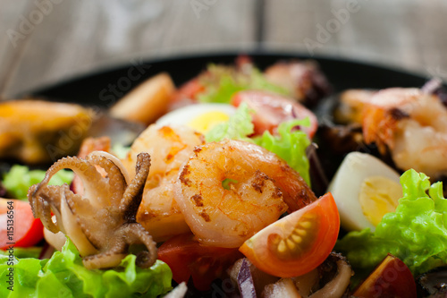 Grilled shrimp, octopus, quail egg in salad closeup. Extreme close-up of grilled seafood salad on wood with quail eggs and tomatoes. Healthy eating, creative food concept