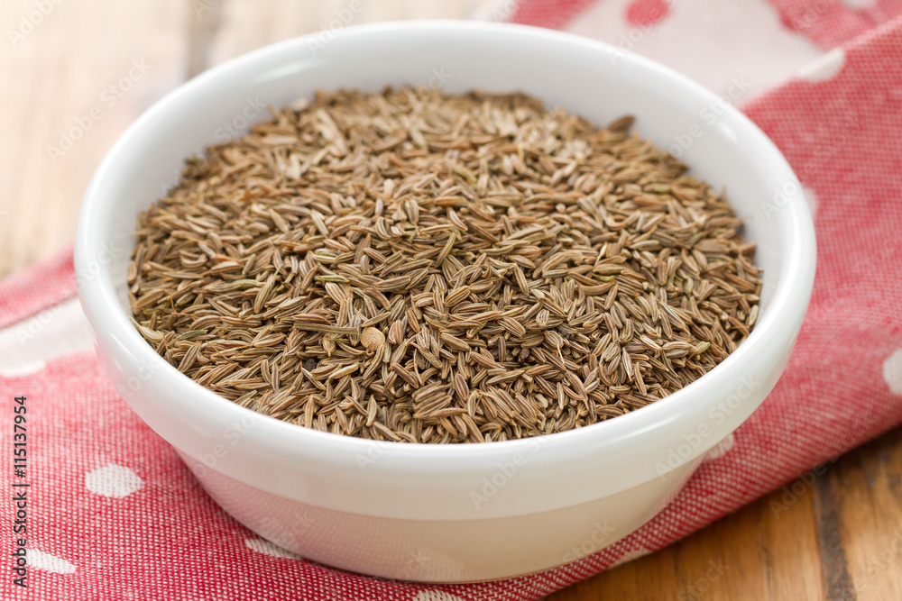 seeds of carum in white bowl on brown background