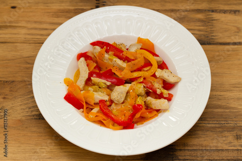 chicken with red pepper and carrot on white plate on brown background