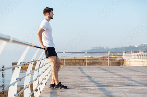 Handsome young man standing on wooden terrace near the sea