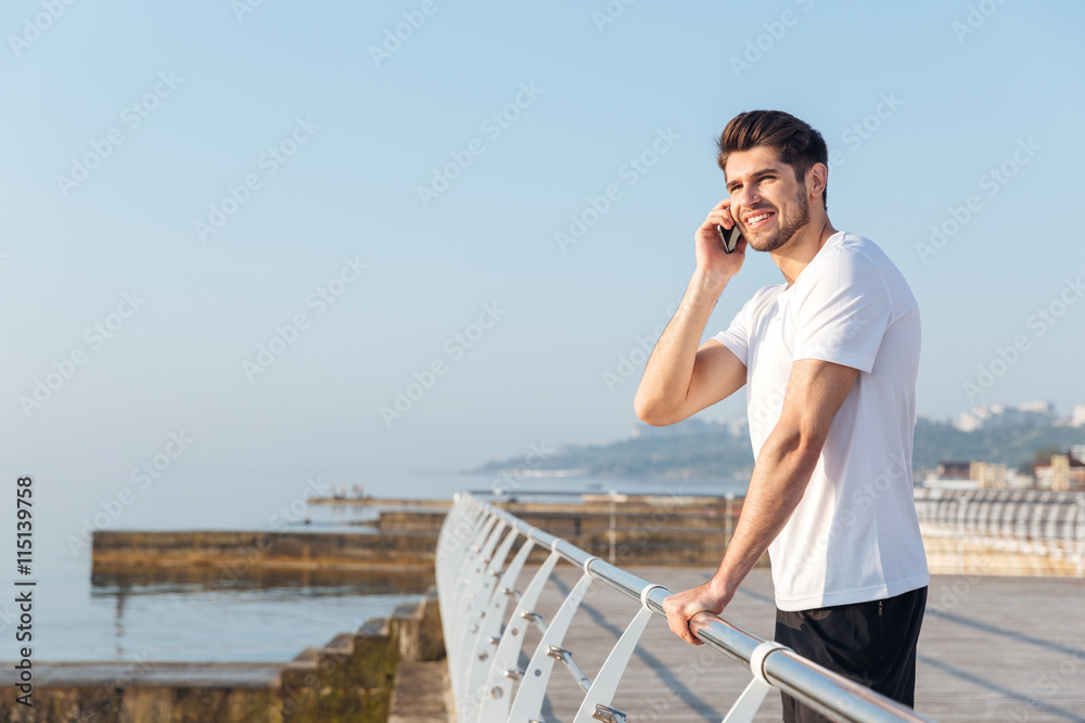 Cheerful young sportsman talking on mobile phone outdoors