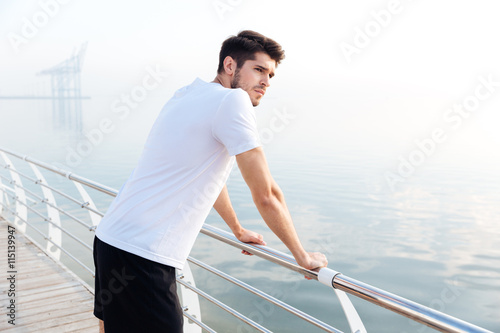Fototapeta Naklejka Na Ścianę i Meble -  Sportsman standing on pier and looking at the sea