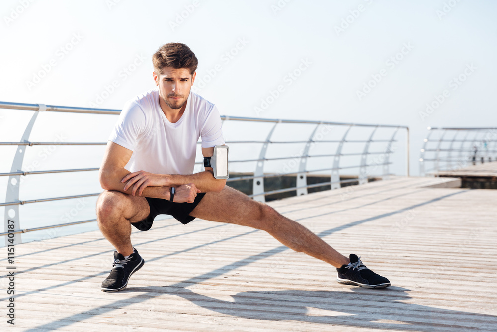 Fotografie Young sportsman stretching legs during workout on pier