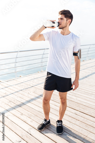 Young sportsman standing and drinking water outdoors