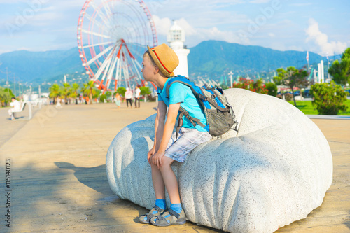 Boy with hat and  backpack  sitting on bench with  park background. Focus on boy. photo