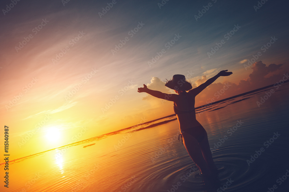 Happy woman watching the sun rising over the horizon at the ocean