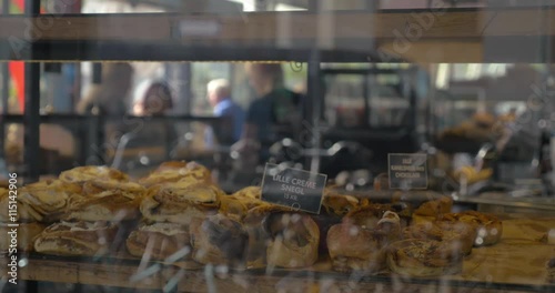 Appetizing buns in the show-window of a bakery. Customers and staff inside, view through the glass