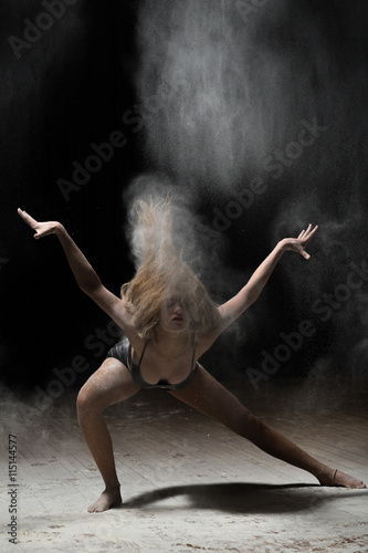 Young ballerina dancing with flour on black background