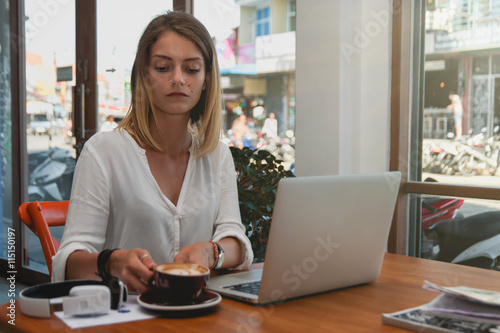 Young attractive freelancer using laptop computer for distance job while sitting in modern coffee shop interior.